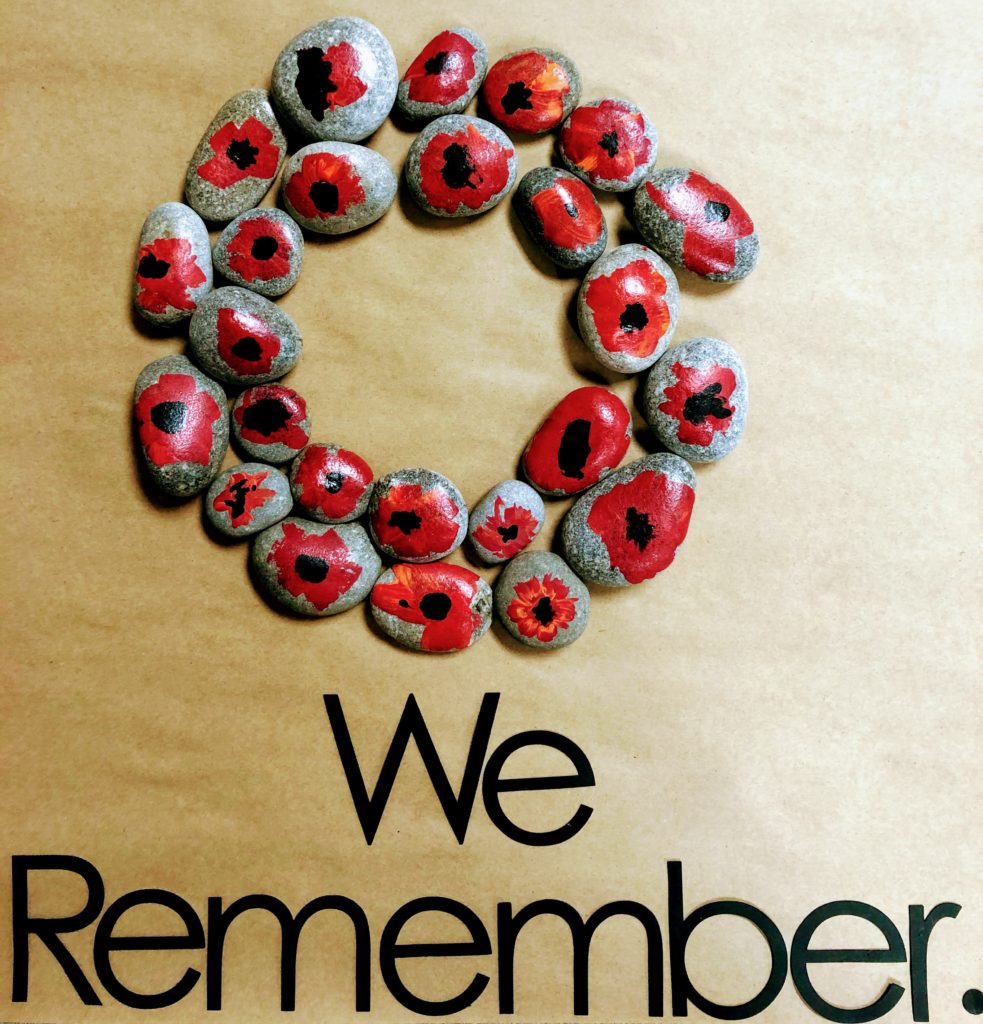 River rocks painted with poppies to observe Remembrance day in Kindergarten formed into a wreath with the words We Remember beneath.